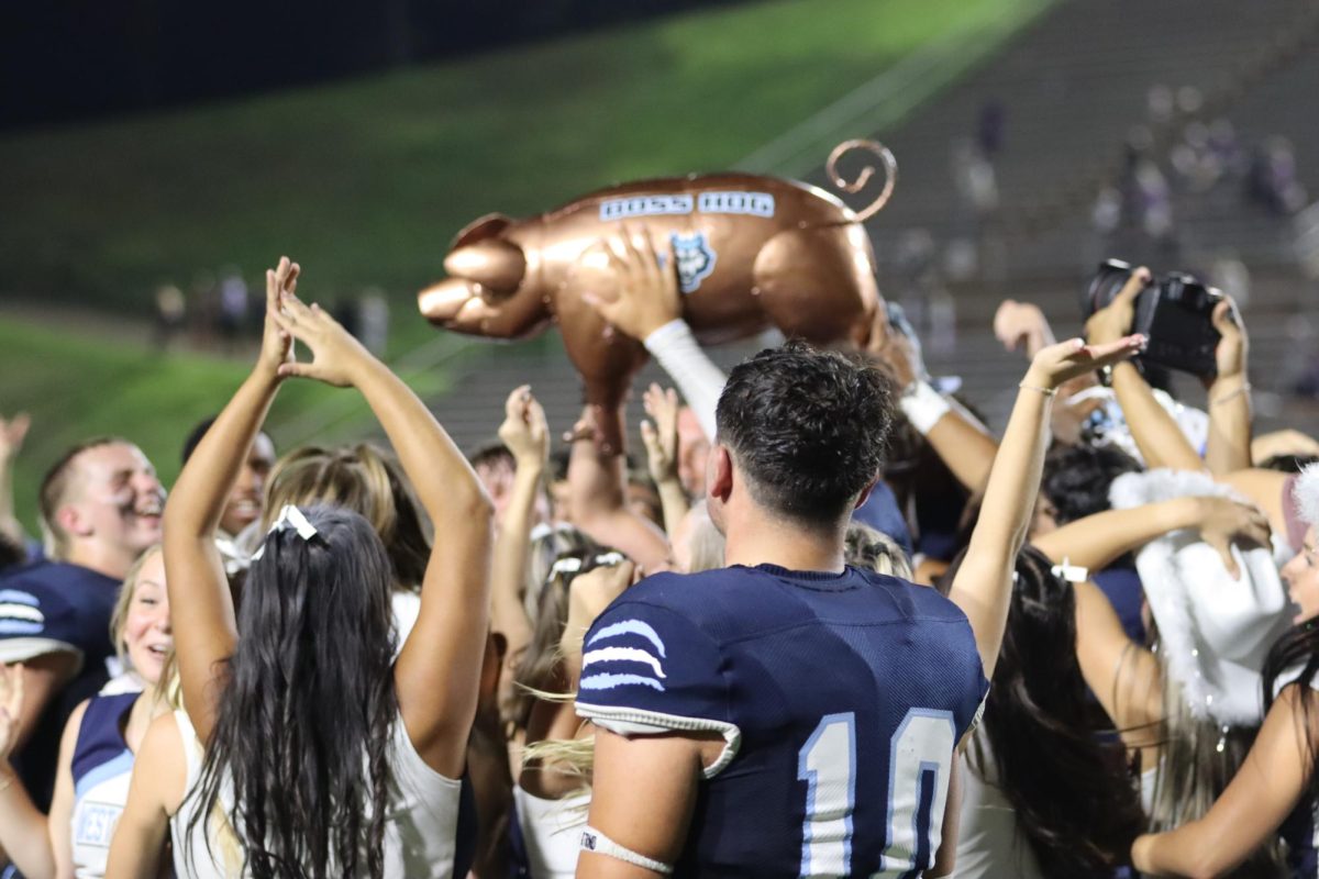Celebrating the big win, football players and cheerleaders raise the hog. 